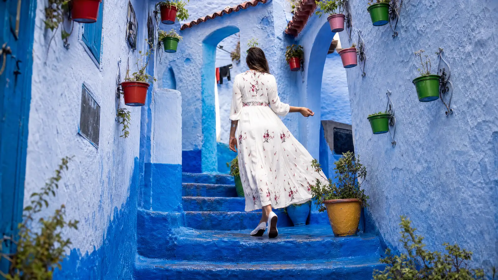 Une voyageuse monte des marches bleues entre les pots de fleurs, à Chefchaouen