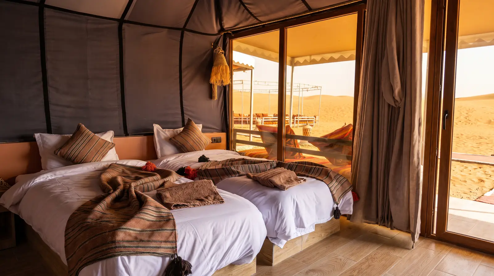 A luxury tent with two beds and a view of the dunes at Merzouga Dunes Luxury Camps